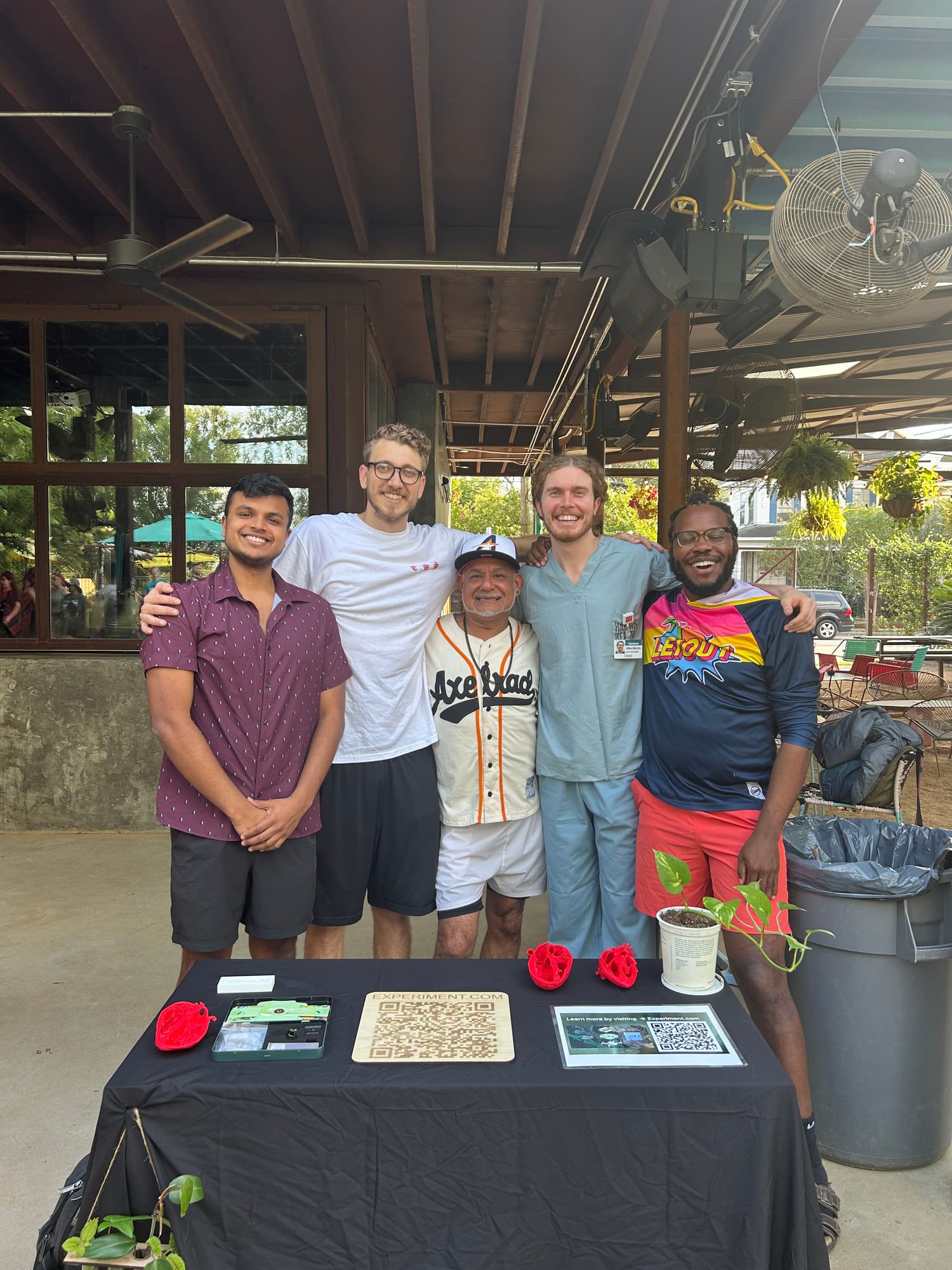 Five team members stand behind a table of Foldscope demos at an outdoor run-club event