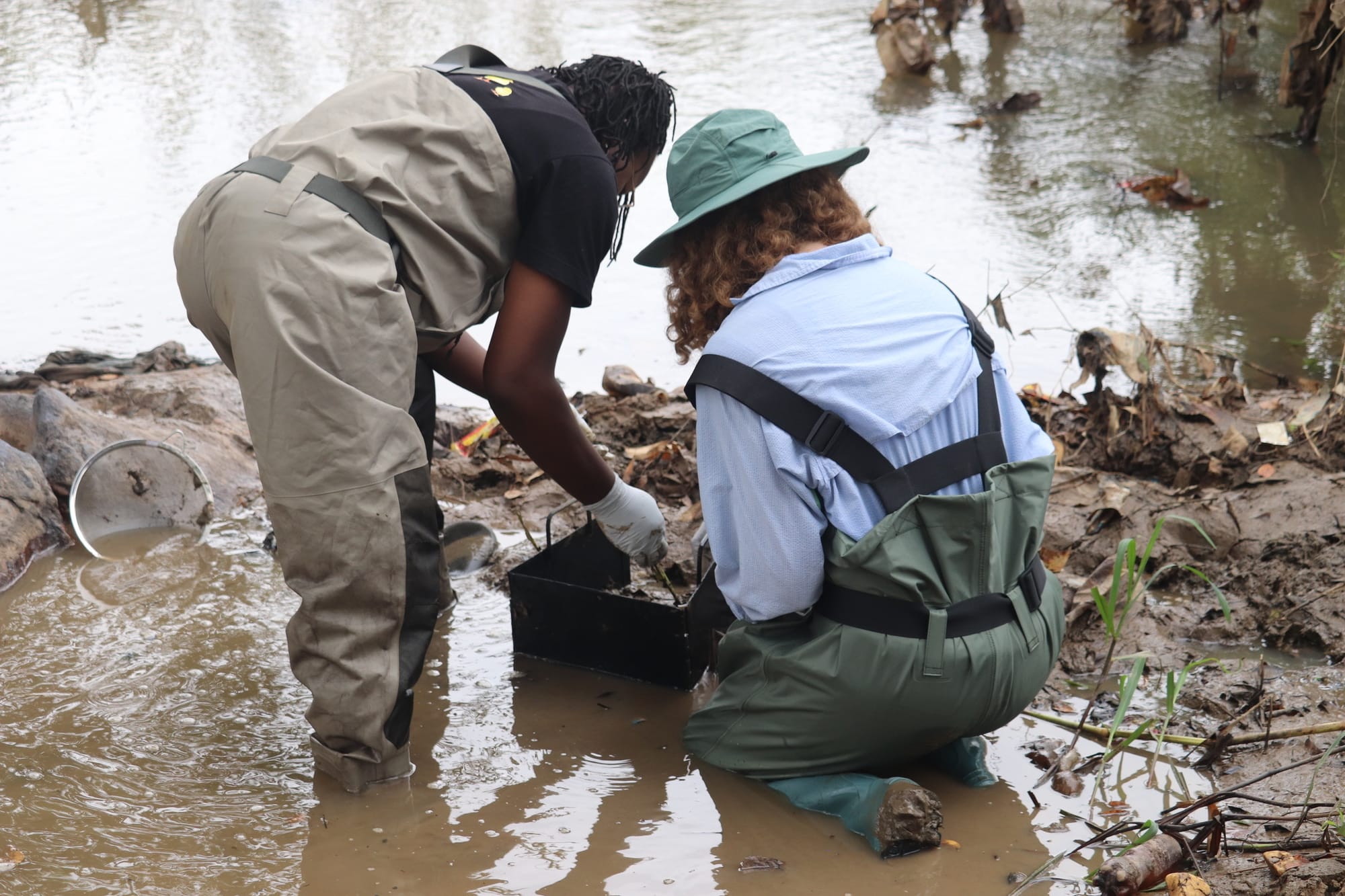 Two researchers in waders lower a welded metal quadrat onto a shallow riverbed