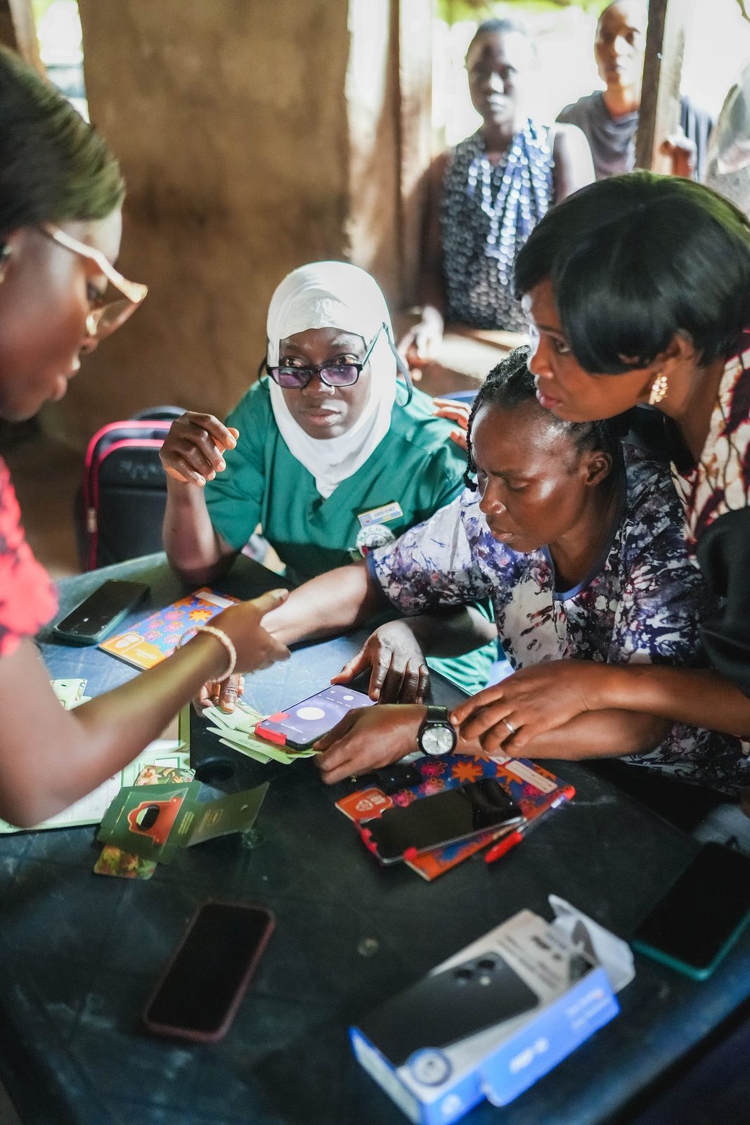 Kareem, a community health worker in green scrubs and a white hijab, learns foldscopy at a table with colleagues in Imala Odo