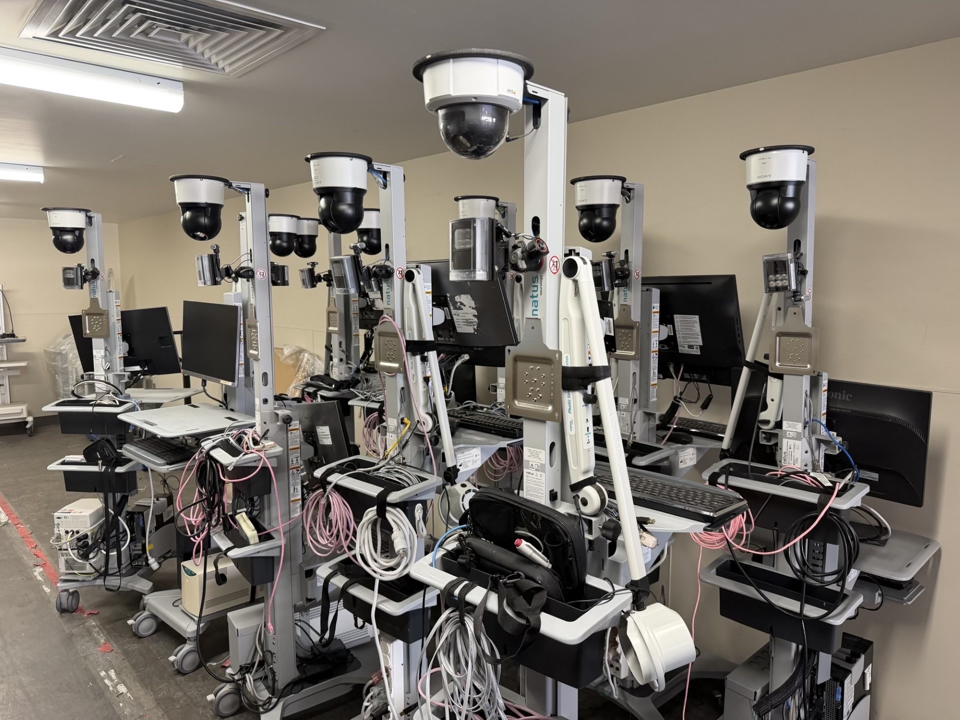 A row of mobile video-EEG monitoring carts — Natus units with overhead cameras, monitors, and bundled electrode leads — staged in a clinical room.