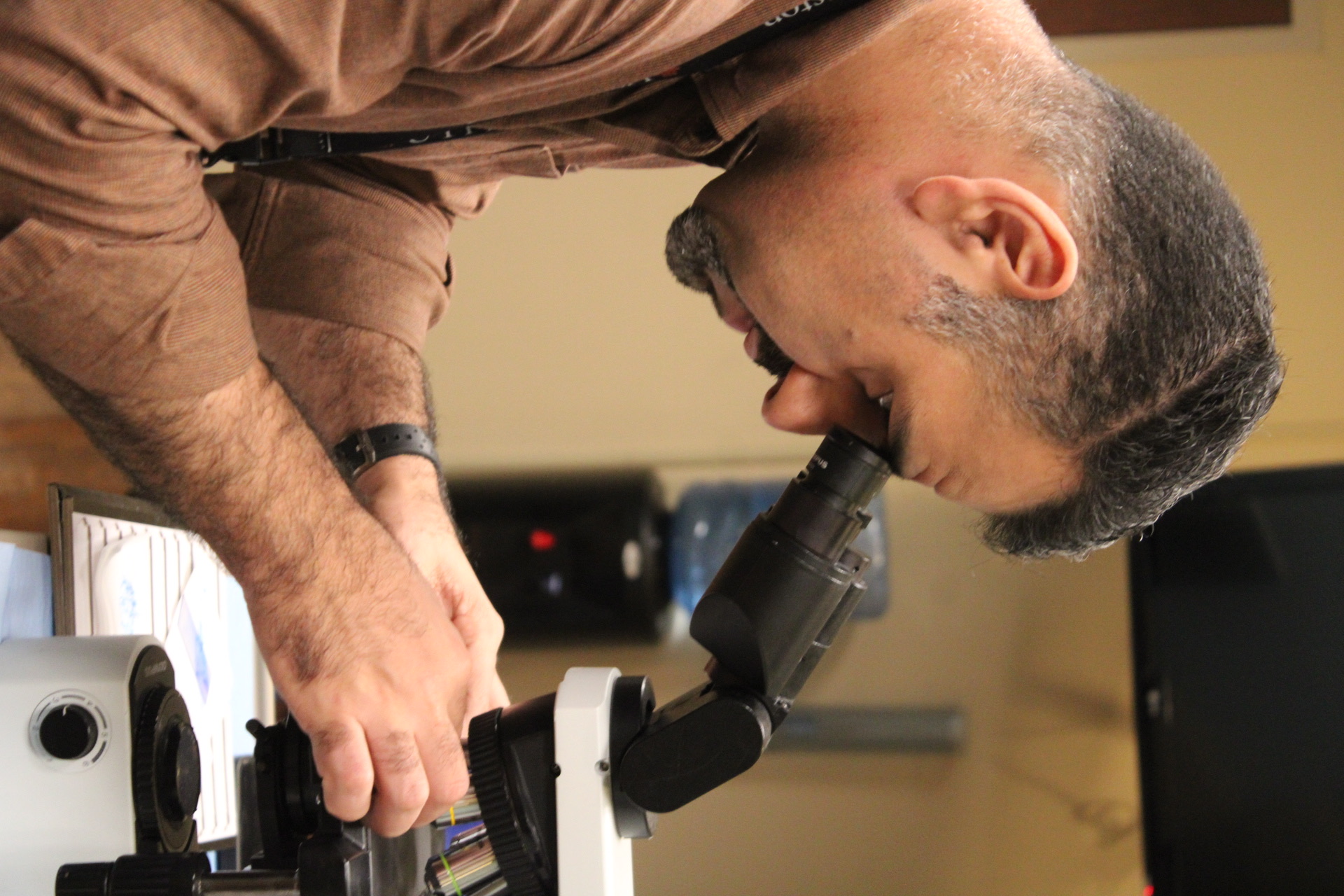 A clinician examining a slide under a microscope while screening samples in the lab